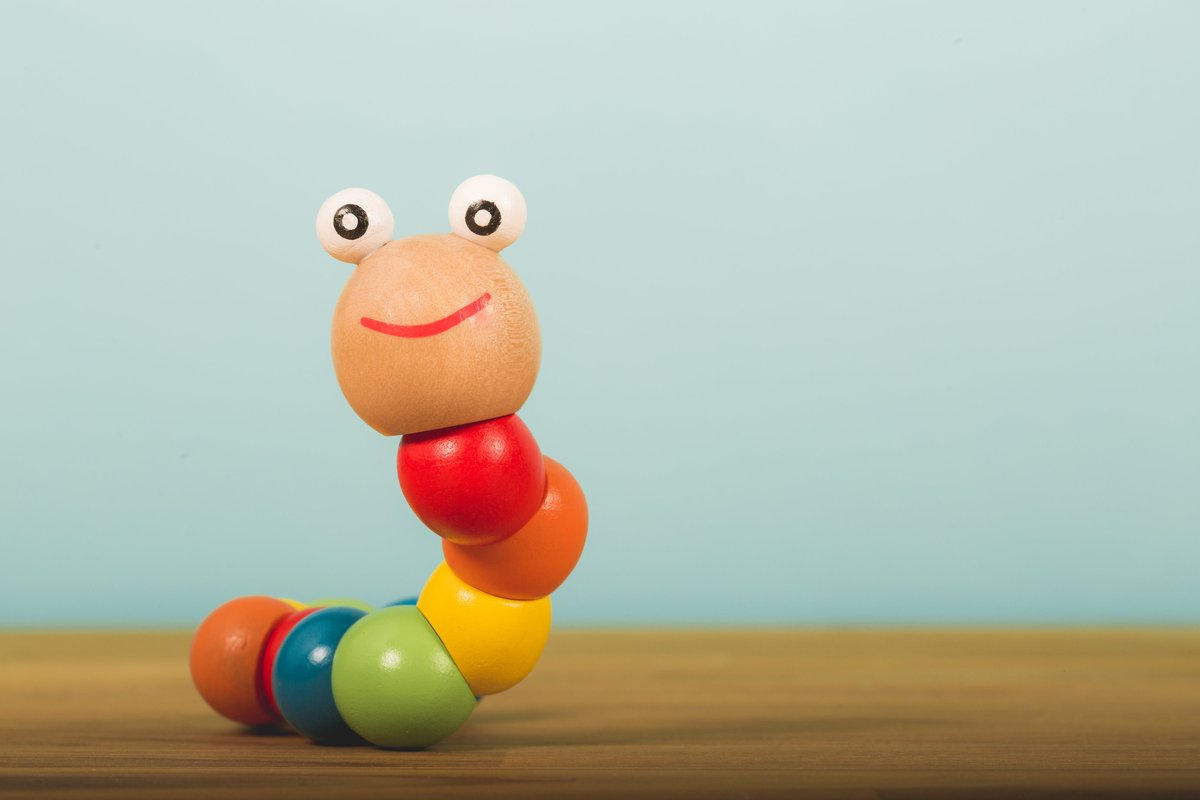 Raw product photo of a colourful wooden worm toy on a table against a plain blue background
